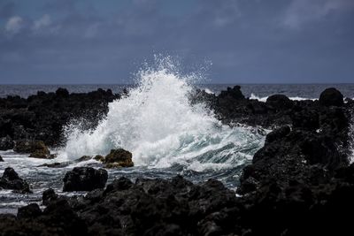 Waves splashing on rocks at shore against sky
