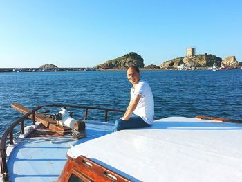 Side view portrait of smiling man sitting on sailboat in sea