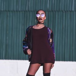 Beautiful woman wearing sunglasses while standing against corrugated iron