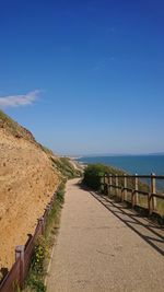 Empty road by sea against blue sky
