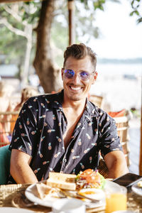 Portrait of smiling man with breakfast on table at resort during sunny day