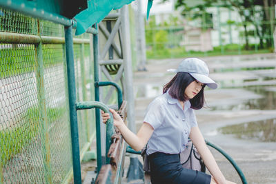 Side view of thoughtful young woman looking down while sitting on bench in park during rainy season