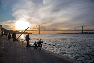 People on suspension bridge over sea during sunset
