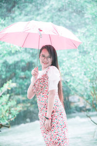 Portrait of smiling young woman holding umbrella standing by river