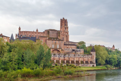 Old building by river against cloudy sky