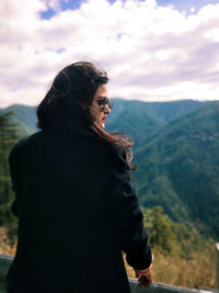 Side view of young woman looking at mountains against sky