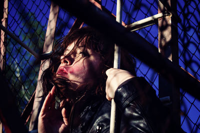 Low angle view of young woman looking through fence