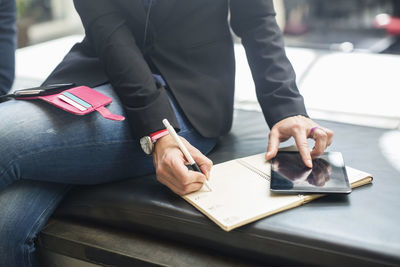 Midsection of businesswoman using digital tablet while writing in book at cafe
