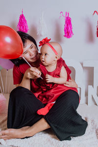 Low section of woman and child sitting with balloons at home