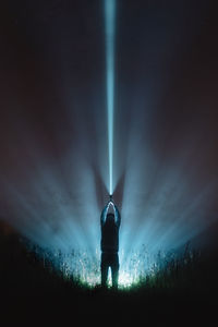 Man with illuminated flash light standing on field against sky at night