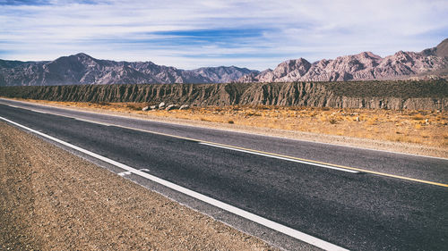 Empty road by rocky mountains against sky