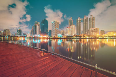 Illuminated buildings by river against sky in city