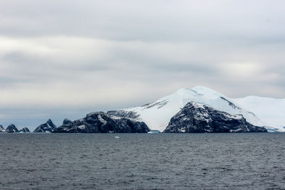 Scenic view of sea by snowcapped mountain against sky