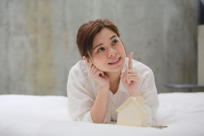 Close-up of smiling woman gesturing while lying on bed with model house