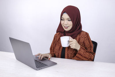 Young woman using mobile phone while sitting on laptop