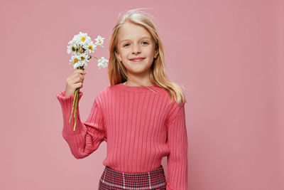 Portrait of young woman holding gift against pink background