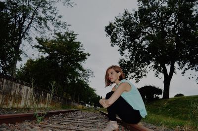 Side view of young woman sitting on railroad tracks at dusk
