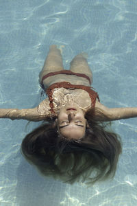 Close up view of young blonde woman upside down relaxing in the surface of the water in the pool