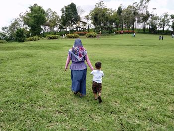 Rear view of mother with son walking on grassy field in park