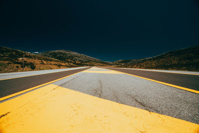 Surface level view of empty country road against clear blue sky