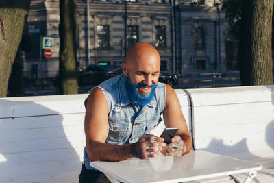 Fashionable man with a blue beard sits at a white table and uses a mobile phone