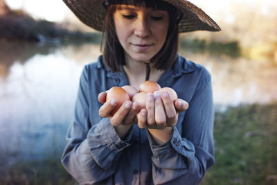 Young female farmer holding eggs while standing on lakeshore
