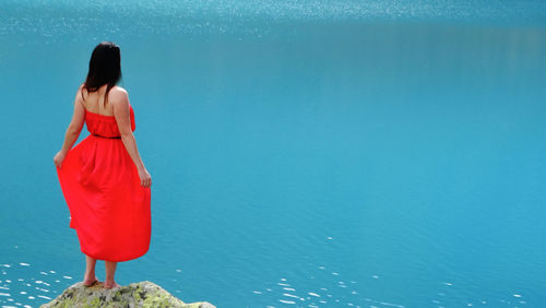 Girl in a red dress on the shore of a blue lake