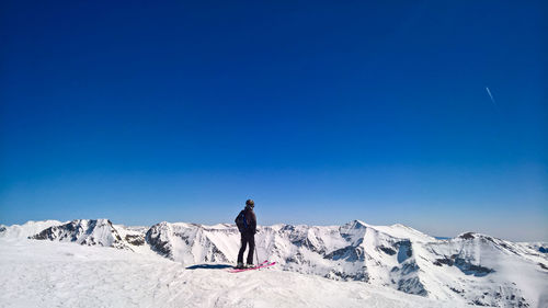 Rear view of person standing on snowcapped mountain against blue sky