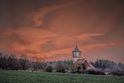 Traditional building on field against sky at sunset