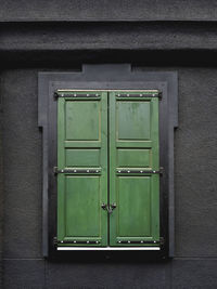 Black wall of building with window locked on wooden green shutters.modern details and vintage style.