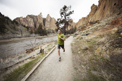 Hiker jogging on footpath by lake against mountains