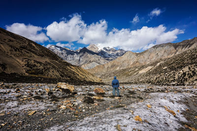 Rear view of man walking on rocks against sky