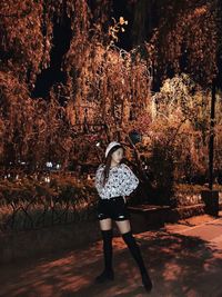 Full length of fashionable woman standing on street by plants at night