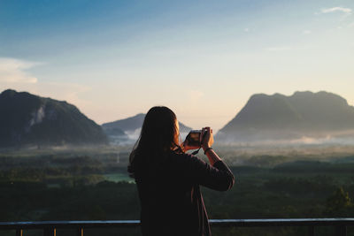 Rear view of man photographing on mountain against sky