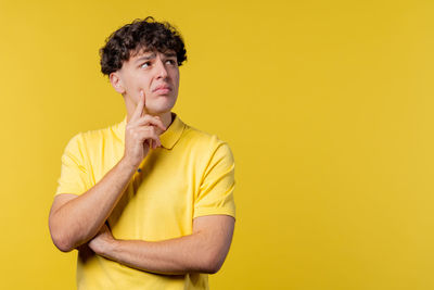 Young man using mobile phone while standing against yellow background