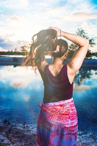 Young woman standing by lake against sky