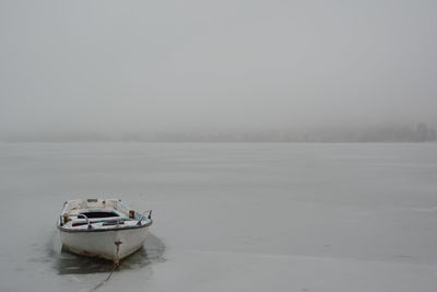 Boat moored on frozen lake against sky