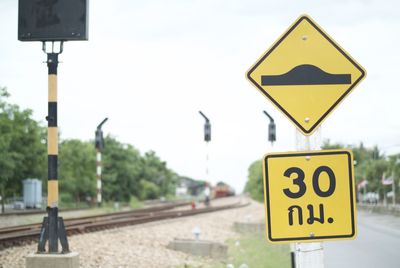 Close-up of speed bump sign by railroad track against sky