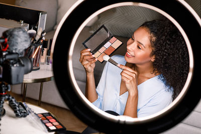 Smiling young woman holding face powder by camera at home