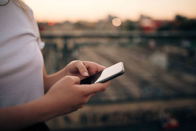 Midsection of young woman using smart phone while standing on bridge in city