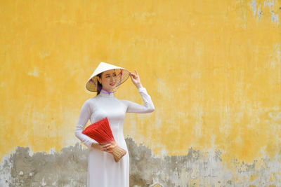 Portrait of young woman standing against wall