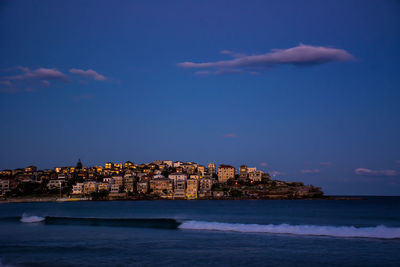 Sea by buildings against sky during sunset