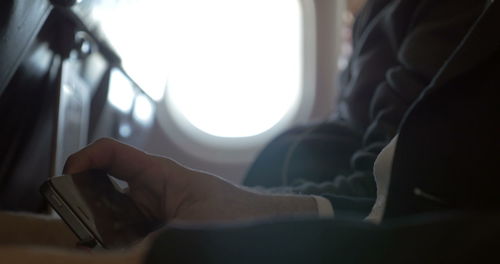 Close-up of hand using mobile phone against window