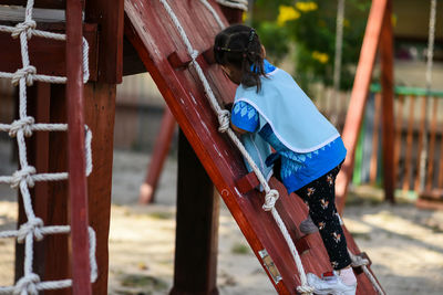 Kindergarten kid girl climb up from wooden slope of kid playground in summer with natural light.