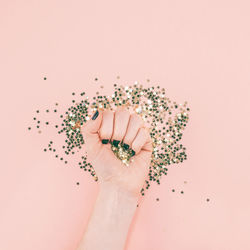 Cropped hand of woman holding sequins against pink background