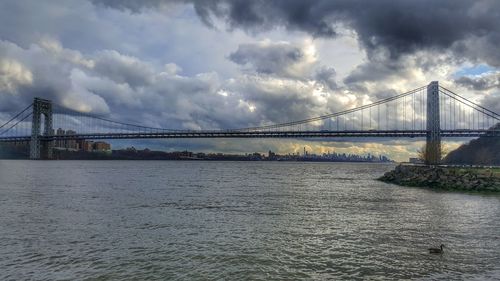 Suspension bridge over river against cloudy sky