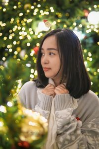 Portrait of young woman standing against christmas tree