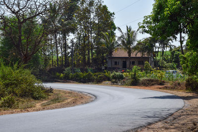 Empty road amidst trees and buildings against sky