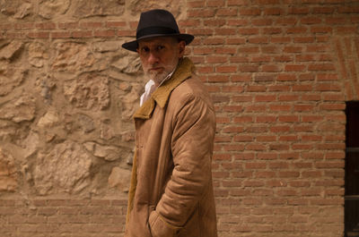 Portrait of adult man in hat and coat against brick wall on street. madrid, spain