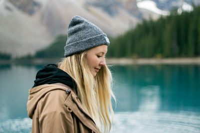 Side view of young woman standing by lake during winter
